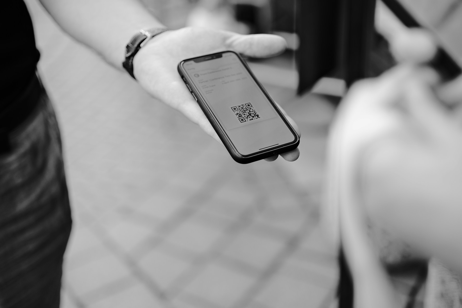A hand holding a phone showing a QR ticket at the entrance to an event